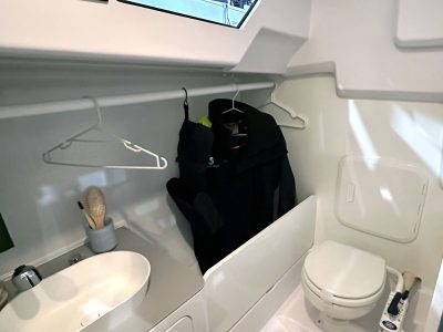 Kleines Bootskabinen-Badezimmer: Waschbecken, Toilette, Jacke an Kleiderstange.