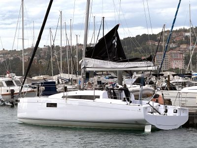 Weißes Segelboot am Kai, weitere Boote im Hafen, Häuser im Hintergrund.
