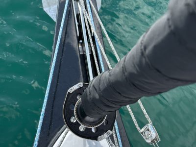 Bug eines Segelbootes mit Takelage, Taue und Winsch, Wasser im Hintergrund.