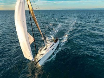Segelboot auf offener See mit weißem Großsegel, Blick von oben aufs Wasser.