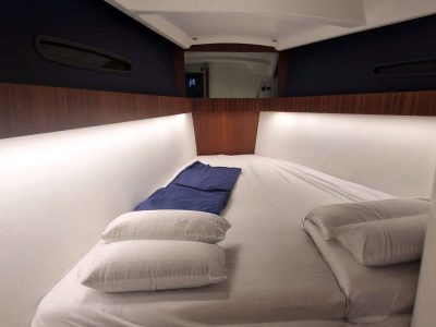 Kleines Kabinenbett mit weißen Laken, zwei Kissen und blauem Kissen, Holzpaneel.