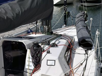 Segelboot im Hafen mit Mast, Taue und gefalteter Segelabdeckung auf dem Deck.